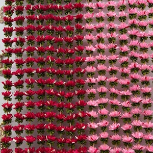 May include: Two strands of artificial flower garlands, one pink and one red, hanging from a silver rod. Each garland is made of small, layered flower shapes with green leaves.