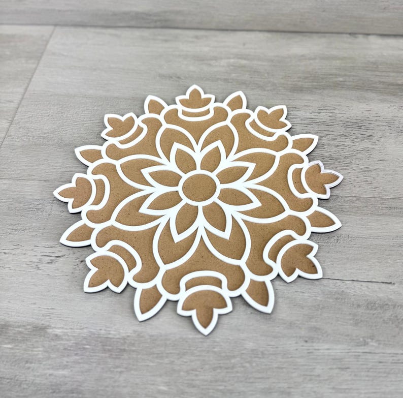 May include: A brown paper mandala with a white intricate design. The mandala is cut out of the paper and has a delicate floral pattern.