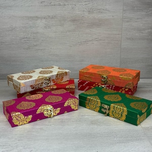 May include: Four decorative boxes with ornate gold designs on a white wood background. The boxes are stacked in a pyramid shape, with the largest box at the bottom and the smallest box at the top. The boxes are made of wood and are covered in fabric with a floral pattern. The boxes have a gold latch on the front.