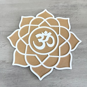 May include: A white om symbol is centred in a brown mandala with a white outline. The mandala is shaped like a flower with eight petals.