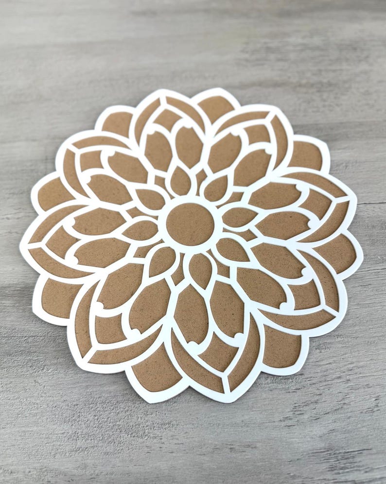May include: A white paper cutout of a mandala design with a brown centre. The mandala has a circular shape and is made up of intricate patterns.