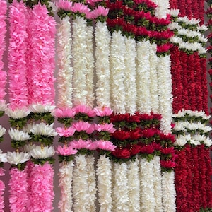 Op de afbeelding: Een display van kleurrijke bloemenslingers in roze, wit en rood. De slingers zijn dicht opeengepakt, waardoor een gestructureerd en levendig visueel effect ontstaat. De bloemen zijn gerangschikt in verticale rijen, geschikt voor feestelijke decoraties.