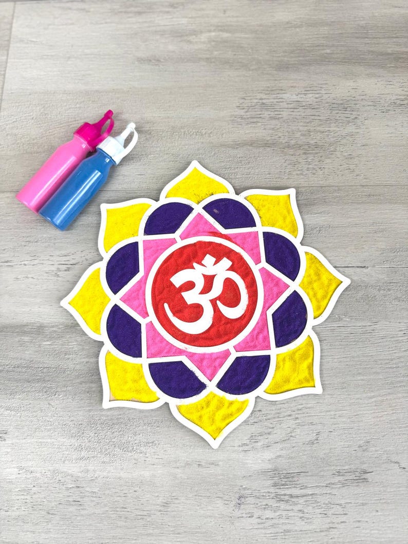 May include: A colourful mandala design with the symbol "Om" in the centre. The mandala is made of yellow, pink, purple, and red sand. Two bottles of paint are in the background.