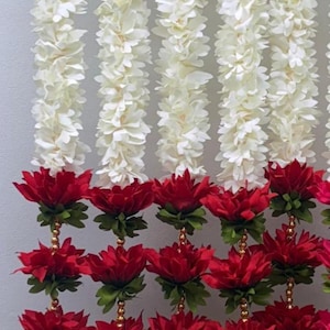 Op de afbeelding: Verticale weergave van bloemenslingers. De slingers zijn voornamelijk wit, met secties van levendige rode bloemen. De witte bloemen hebben een gelaagd bloemblaadjesontwerp. De rode bloemen zijn geaccentueerd met groene bladeren en gouden kralen.