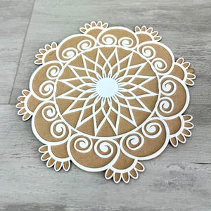 May include: A white mandala design on a brown background. The mandala has a circular pattern with intricate details.