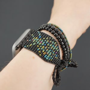 May include: A black beaded watch band with colorful accents. The band is worn on a wrist with other black beaded bracelets.