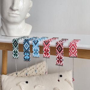 Puede incluir: Seis pulseras de cuentas con diferentes patrones geométricos en rojo, azul, verde y blanco. Cada pulsera tiene una cadena plateada con una pequeña cuenta al final.