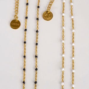 May include: Gold-colored necklaces with beaded accents. One necklace features black beads, another white beads, and a third necklace is visible. Each necklace has a gold-colored chain and a circular charm with the word "OSIDE" or a palm tree design.