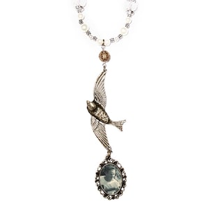 May include: A silver charm necklace with white pearl beads, a silver bird charm, and a silver oval frame with a black and white photo inside.