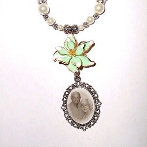 May include: A white pearl and silver beaded chain with a green flower charm and a silver oval frame with a black and white photo of an older couple.