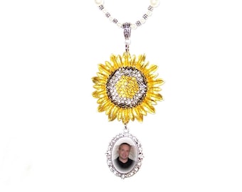 May include: A gold sunflower charm with rhinestones hangs from a beaded necklace with white and green beads. A silver oval locket with a photo of a man is attached to the bottom of the sunflower charm.