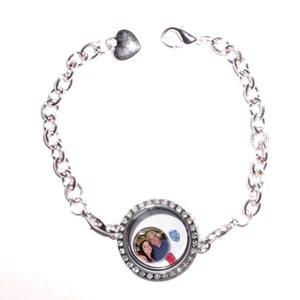 May include: A silver locket bracelet with a heart charm and a photo of a couple inside the locket. The locket is surrounded by clear rhinestones.