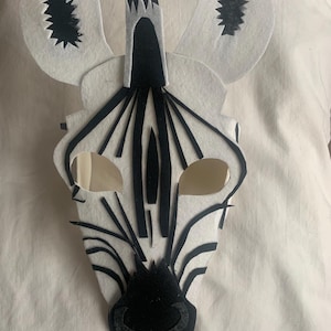 Könnte beinhalten: Eine schwarze und weiße Filz-Zebra-Maske mit schwarzen Filzohren und einer schwarzen Filzmähne. Die Maske hat ausgeschnittene Augenlöcher.