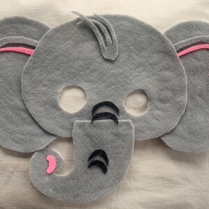 Può includere: Maschera di elefante in feltro grigio con orecchie in feltro rosa e dettagli in feltro nero. La maschera ha fori per gli occhi e la bocca.