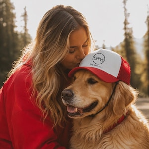 Puede incluir: Gorra de camionero roja y blanca con la palabra "LOVE" y un diseño de huella de pata. La gorra la lleva un golden retriever. El texto "Dog Mom Era" está impreso en la gorra. El perro lleva un collar rojo.