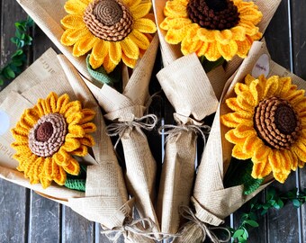 Puede incluir: Un ramo de cinco girasoles de crochet envueltos en papel marrón. Los girasoles son amarillos con centros marrones y tallos verdes.
