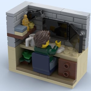 May include: A Lego minifigure sits at a desk with a computer monitor, keyboard, and a cup. The desk is made of Lego bricks and has a drawer. The minifigure is wearing a green shirt and blue pants. The background is a brick wall.