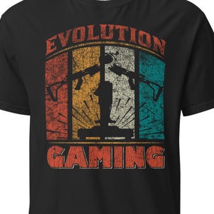 Könnte beinhalten: Ein schwarzes Kurzarm-T-Shirt mit einem abgenutzten Grafikdruck und dem Text EVOLUTION GAMING. Das Design zeigt einen Hintergrund im Retro-Stil mit vertikalen orangefarbenen, gelben und türkisfarbenen Streifen sowie Silhouetten von zwei Gewehren und einem Controller.