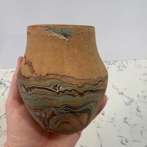 May include: A handcrafted, small, brown pottery vase with a unique, swirled pattern of brown, teal, and cream colors. The vase has a rounded body and a slightly flared rim, showcasing a rustic aesthetic.