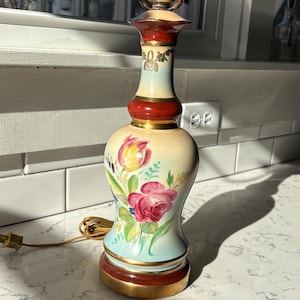 Vintage handpainted table lamp with floral art and gold painted details. 22in tall to top of harp. newer cord works well. Good condition.