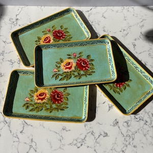 May include: Four rectangular serving trays with a light teal background and floral designs. The trays have a yellow border and a decorative black and white pattern. The floral design features red and yellow roses with green leaves.