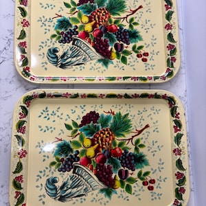 May include: Two rectangular serving trays with a cream-colored background and a colorful fruit design. The trays feature a border of red berries and green leaves. The fruit design includes grapes, pears, and a pineapple.