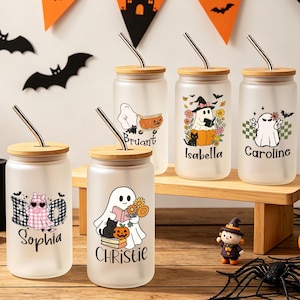 Może przedstawiać: Pięć szklanek z matowego szkła z bambusowymi pokrywkami i metalowymi słomkami, każda z unikalnymi grafikami halloweenowymi przedstawiającymi duchy, dynie i koty. Na szklankach nadrukowano imiona Sophia, Christie, Bruant, Isabella i Caroline.