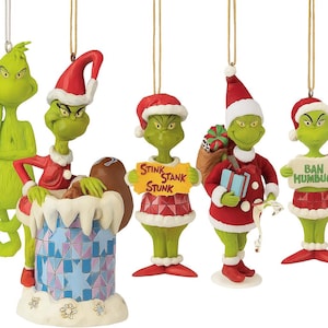 May include: A set of Christmas tree decorations depicting the Grinch. The ornaments are predominantly green, with red and white detailing, such as Santa hats and clothing. Some hold signs with the phrases "Stink Stank Stunk" and "Ban Humbug".