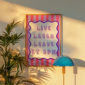 Könnte beinhalten: Ein gerahmter Druck mit einem rosa-weiß gestreiften Hintergrund und dem Text "Live Laugh Leave By 9pm" in lila Buchstaben.