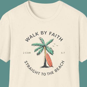Op de afbeelding: Crèmekleurig T-shirt met een cirkelvormige afbeelding van een palmboom, een surfboard en de tekst "WALK BY FAITH STRAIGHT TO THE BEACH" met bijbelverwijzingen. Het ontwerp bevat groene, rode en zwarte elementen.