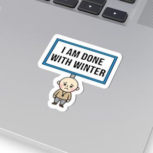 May include: A sticker featuring a cartoon figure holding a sign that reads "I AM DONE WITH WINTER." The figure has a sad expression and is wearing a tan jacket and gray pants. The sign has a blue border.