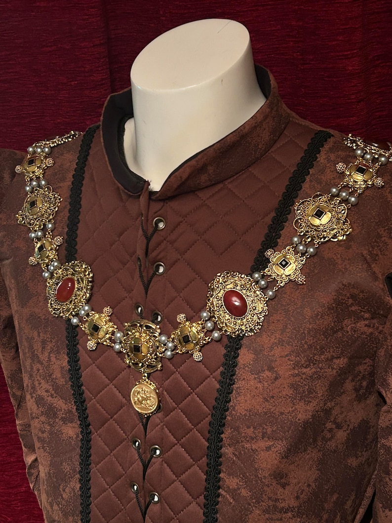 May include: A brown quilted jacket with a black lace trim and a gold and red jeweled necklace. The necklace has a large pendant with a detailed design.