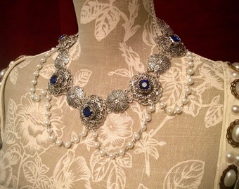 May include: A silver filigree necklace with blue gemstone accents and a pearl strand.
