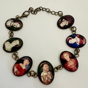 May include: A bronze chain bracelet with oval-shaped charms featuring portraits of historical figures. The charms are set against a white background and have a vintage aesthetic.
