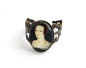 May include: A bronze ring with an oval cameo featuring a portrait of a woman in a white lace collar and black dress.
