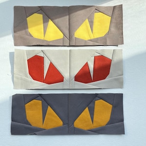 May include: Three fabric panels with a patchwork design of eyes. The top panel is gray with yellow eyes, the middle panel is white with red eyes, and the bottom panel is dark gray with orange eyes.