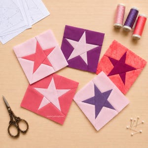 Pode incluir: Cinco blocos de tecido quadrados para acolchoado com padrões de estrelas em tons de rosa, roxo e coral. O conjunto inclui três carretéis de linha em rosa, roxo e vermelho, uma tesoura de metal ornamentada e moldes de costura em papel.