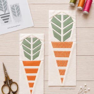Könnte beinhalten: Zwei Stoff-Quiltblöcke in Karottenform mit grünen Blättern und orangefarbenen Wurzeln, begleitet von einem Schnittmusterbogen mit der Aufschrift PLANT POTS BLOCKS 2 SIZES 6" x 12" 4" x 8", drei Garnrollen, einer Schere und Nähnadeln.