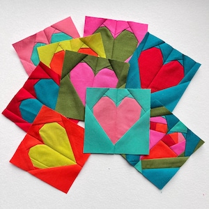 Könnte beinhalten: Neun Stoffquadrate mit einem Herzdesign in verschiedenen Farben, darunter Rot, Rosa, Grün, Gelb und Blau. Jedes Quadrat besteht aus einem anderen Stoff und hat ein einzigartiges Herzdesign.