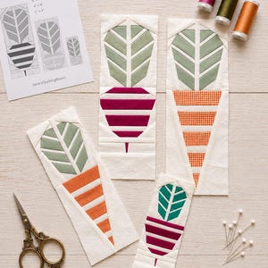 May include: Four fabric quilt blocks featuring plant and pot designs in various colors including green, magenta, and orange. The blocks are accompanied by a printed instruction sheet labeled PLANT POTS BLOCKS with sizes 6x12, 4x8, and 2x4 inches, along with sewing scissors, three spools of thread, and several sewing pins.