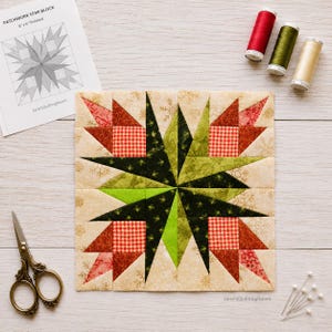 May include: A square patchwork star quilt block featuring a central dark green and lime green star surrounded by red, white, and cream fabric pieces with snowflake patterns. Includes a pattern sheet, three spools of thread, and metal scissors.