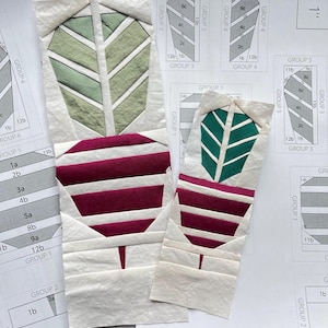 Może przedstawiać: Dwa bloki do pikowania w kształcie pióra z tkaniny z zielonymi i bordowymi akcentami, na tle szablonów wzorów. Bloki są białe z zielonymi i bordowymi wzorami liści. Szablony mają schematy i wymiary.