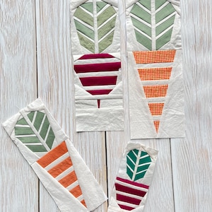May include: Four fabric art pieces featuring stylized vegetable designs. The pieces include green leaves, and red or orange vegetable bodies. The pieces are arranged on a light wood grain surface.