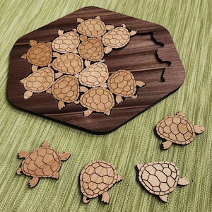 Op de afbeelding: Houten puzzel met een zeshoekig bord met een uitsnijding van een groep schildpadden. Het bord is gemaakt van donker hout en de schildpadden zijn gemaakt van licht hout. Er zijn vijf extra schildpadstukken die op het bord kunnen worden geplaatst.
