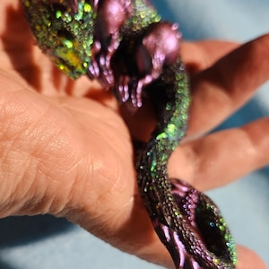 May include: A small, iridescent purple and green dragon figurine with a glittery finish. The dragon is curled up with its tail wrapped around its body.