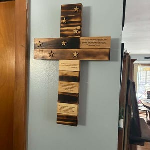 May include: A wall-mounted wooden cross with a scorched finish, featuring seven attached wooden stars. The cross displays printed Bible verses including Jeremiah 29:11, Proverbs 3:6, Matthew 28:19, and John 3:16 on the horizontal and vertical segments.