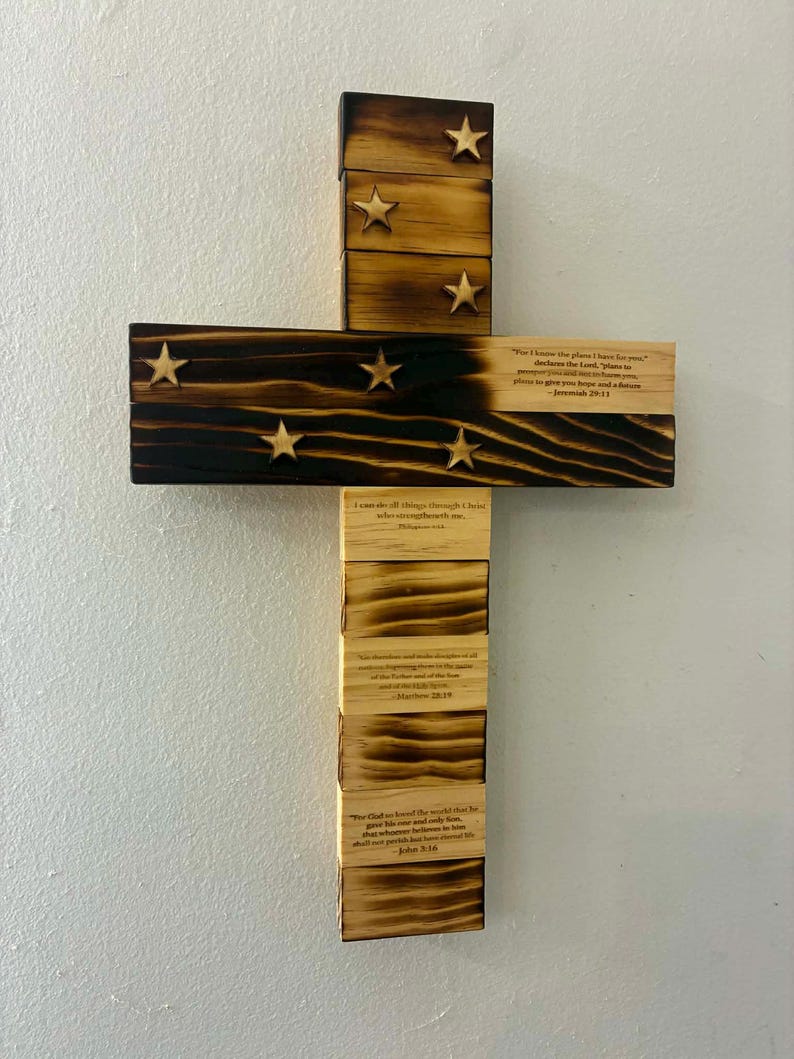 May include: A wooden cross wall decoration featuring a burnt wood finish on the upper section with six attached wooden stars. The lower section is light-colored wood with printed Bible verses including Jeremiah 29:11, Philippians 4:13, Matthew 28:19, and John 3:16.