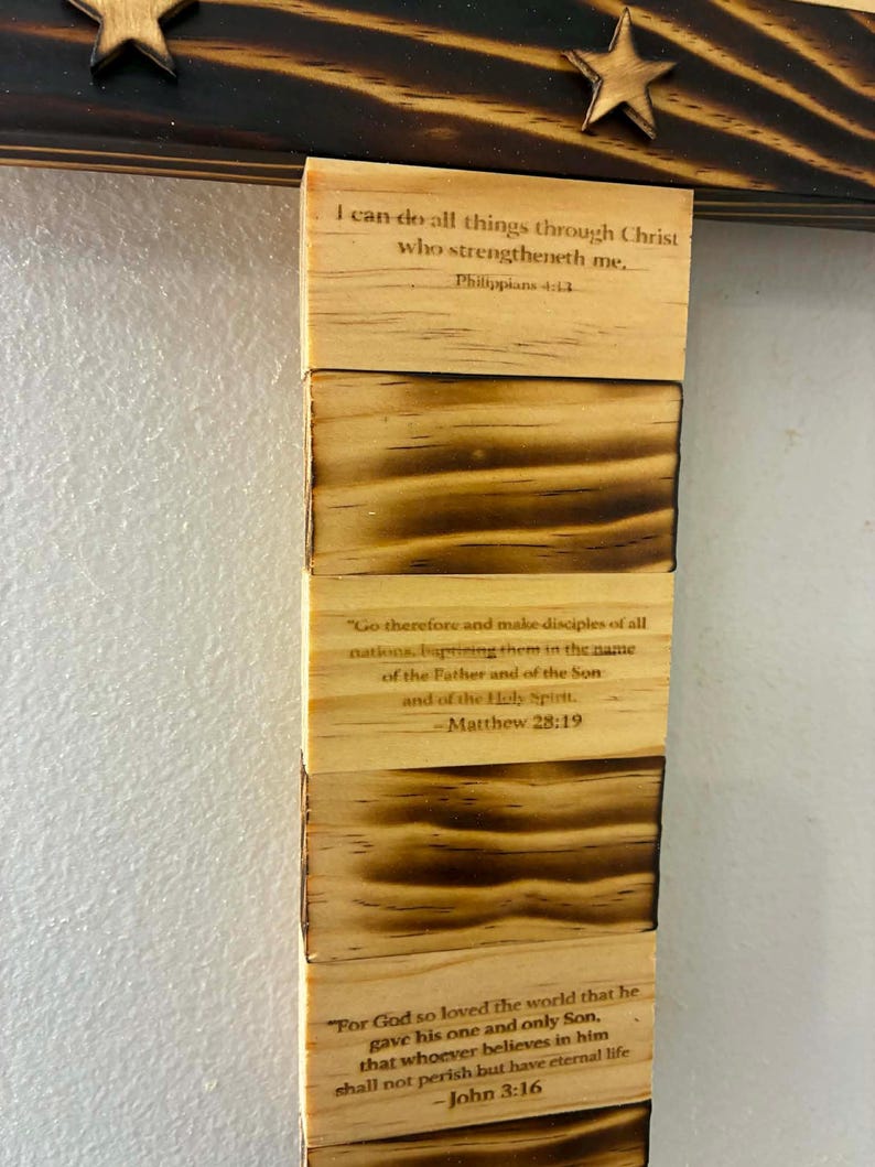 May include: A vertical wooden wall hanging featuring alternating blocks of light natural wood and scorched dark wood. The light blocks are printed with Bible verses: Philippians 4:13, Matthew 28:19, and John 3:16. A dark wooden crossbar with stars sits above.