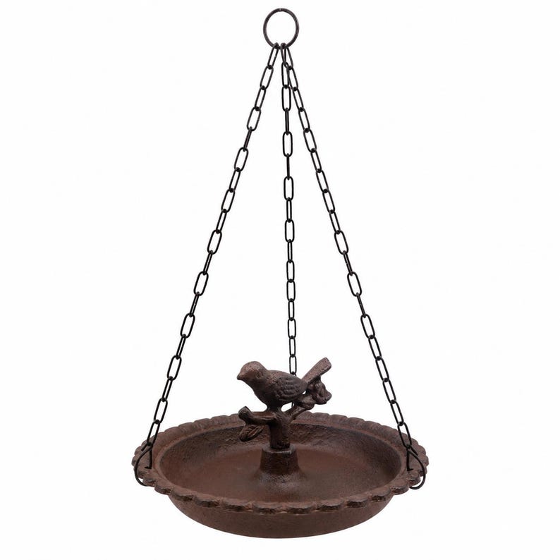 Op de afbeelding: Een hangende vogelvoederbak van donkerbruin gietijzer met een ronde schaal met een geschulpte rand en een centrale paal met een kleine vogel op een tak. De voederbak wordt opgehangen aan drie dunne zwarte metalen kettingen aan een ring.