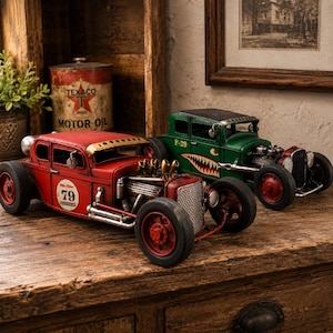 May include: Two metal model hot rod cars, one red with the number 79 and one green with a shark mouth graphic and P-29 text. Both vehicles feature exposed engines, large black wheels, and detailed chassis components, displayed as decorative items.